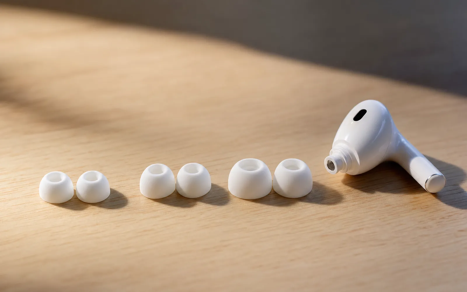 Three sizes of silicone ear tips laid out beside a wireless earbud with its tip removed