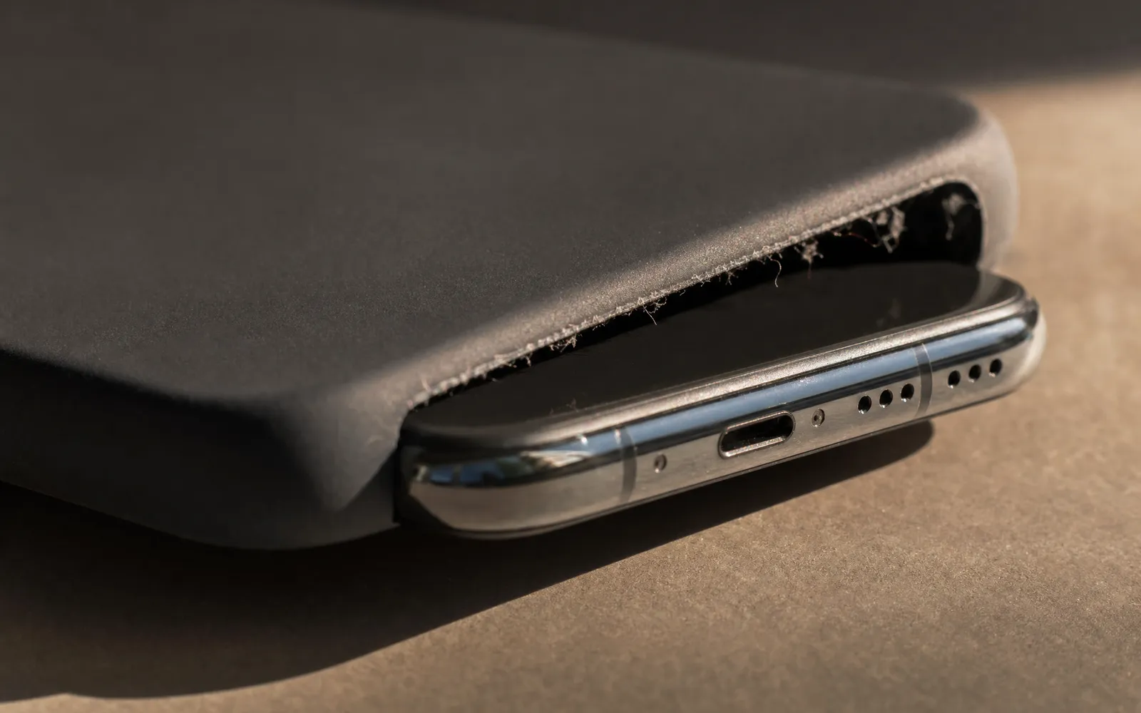 A phone half out of a silicone case, with grey lint gathered along the case's bottom cutout